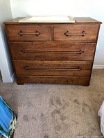 Front view of vintage wooden dresser with four drawers and wooden handles. Mirror resting on top.