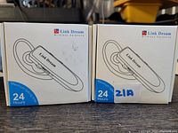 Photo showing two boxed Link Dream Wireless Single Earphones with Microphone, highlighting brand, packaging, and claim of 24-hour maximum talk time per earphone.