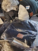 Photo of 4 winter Bluetooth toques showing two black knit fleece-lined toques with leather-like patches and two gray fuzzy water-repellent toques with ear flaps and face masks, some packaged in plastic.