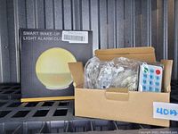 Smart Wake-Up Light Alarm Clock box with LED time display and accessories including curtain lights with remote control in an open box next to it.