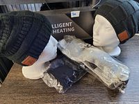 Two mannequins wearing black fleece-lined Bluetooth toques with leather-like patches. Two pairs of packaged heated socks in grey and black with battery packs and chargers laid in front.