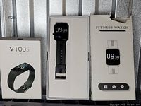 Two black silicone fitness watches in their original packaging, one open displaying the watch face and one closed in a labeled box.