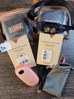 Two black Slonik headlamps with adjustable straps behind two boxed and unboxed peach-colored rechargeable handwarmers, USB cable and protective sleeves.