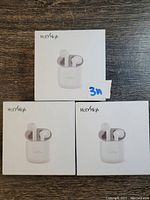 Three boxed Holy High wireless earbuds visible in original packaging, arranged in a triangular formation on a wooden surface.