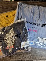 Photo showing black holey tank top and blue turtle neck dress in plastic packaging with Jed North Apparel branding visible