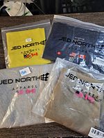 Four Jed North apparel items in original packaging, folded, all size XS.