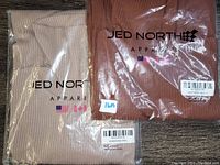 Two Jed North branded dress packages, one tan and one burgundy, each labeled with size information.