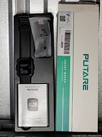 New Putare black silicone smart watch in original gray plastic tray within packaging box. Charging cable and operating instructions manual included.