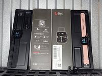 Two Orit brand smart watches with original packaging, one with a black strap and one with a pink strap, both showing time 23:56 on their digital displays