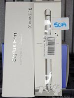 Photo shows two white stylus pens fully boxed in white packaging labeled 'Stylus Pen' with certification marks. One box has a barcode sticker.