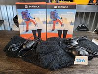 Two pairs of Bernuly electric heated socks in branded boxes with cords and control switches laid out on a dark wood surface.