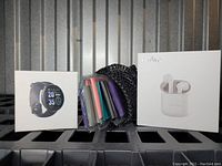 Photo showing all three items: boxed black smart fitness watch, package of colorful resistance/tension bands in mesh pouch, and white box containing Holy High true wireless earbuds with charging case.