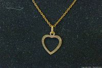 Close-up of gold open heart pendant showing detailed edges and attachment to chain.