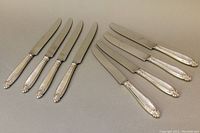 Eight sterling silver handle knives arranged in two groups showing the full length of the knives.