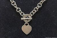 Close-up of the toggle clasp and heart charm pendant showing details of the links and charm shape.