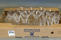 Top view of assorted crystal glasses in cardboard box showing various cut patterns and types of glasses including tumblers and stemware.