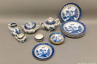 Full set showing teapot, sugar bowls, creamer pitcher, luncheon plates, dessert plate, and dessert bowls with blue and white willow design accented by gold trim.