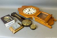 Overview of the wooden Kienzle wall clock with attached Gischard hygrometer and barometer instruments, alongside additional smaller clocks and a boxed clock component