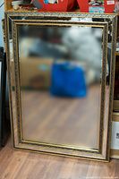 Full view of the mirror leaning against a wall showing the ornate gold and black frame.