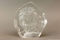 Front view of the clear crystal paperweight featuring the frosted lion's head sculpture inside, showcasing the detailed mane and facial features of the lion.