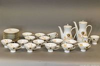 Full set showing teacups, saucers, coffee pot, teapot, creamer, sugar bowl, all decorated with a gold and brown rose floral pattern on white porcelain.