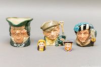Front view showing three Royal Doulton toby mugs with character faces and two Staffordshire thimbles in front.