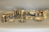 Full view of all silver plated servingware items arranged in one line, showing chafing dish, candleholder, goblets, salt and pepper shakers, bowls, trays, and other pieces.