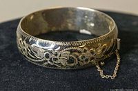Front view of the sterling silver bangle showing detailed etched floral designs and safety chain attached.