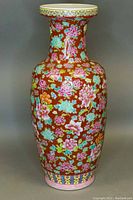 Front angle of tall hand painted floor vase showing detailed floral pattern and flared neck on red-brown background.