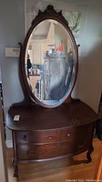 Full view of the antique wooden dresser with attached oval mirror showing drawers and cabriole legs.