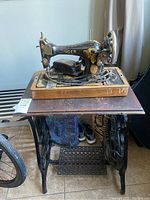 Antique Singer sewing machine mounted on wood table with cast iron treadle base, showing overall condition and structure