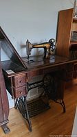 Side view of antique Singer sewing machine mounted in wooden cabinet with treadle base.