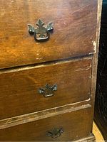 Close up of three drawers on the antique wooden desk with decorative metal handles and visible wear on wood surface.