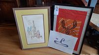 Framed abstract figure print with yellow mat, framed lobster print with orange background, and original swan artwork unframed in front