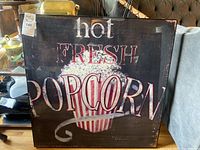 Front view of framed art print featuring 'hot FRESH POPCORN' text and popcorn illustration with visible frame damage.