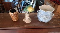 Image showing all three items together on a wooden surface: beige base Beswick parakeet figurine in the center, small brown vase on left, larger white decorative ceramic vase on right.
