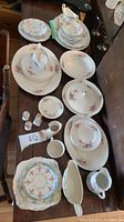 Full set of ceramic dishes arranged on table showing plates, bowls, platters, creamer, gravy boat, and small items with floral design.