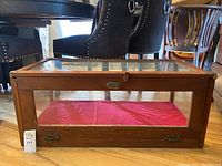 Front side of the wooden and glass display case showing red fabric lining inside and metal spring latches.