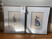 Two framed Indigenous art etching prints by Richard Shorty side by side on wooden surface, showing full front with silver frames and double matting.