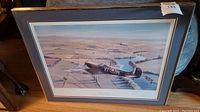 Framed art print showing Spitfire airplane flying over a landscape, with RAF codes visible, and mat framing.