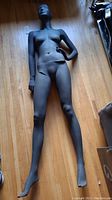 Full-length image of the gray female mannequin laying on the wooden floor, showing overall condition and pose with one hand on hip.