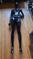 Full length view of black female mannequin laying flat on wooden floor, glossy surface, tape visible around waist.