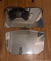 Top-down photo of both vintage hanging mirrors on a wooden floor, showing the size and edges including cracks and damage.
