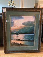 Framed art print showing the scenic lakeside image with boat, mountains, and birds, with visible frame wear.