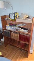 Front view of wooden shelving unit with shelves containing books, boxes, tools, and miscellaneous items.