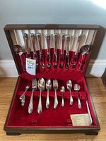 Open flatware case showing knives on top half and other utensils in red velvet slots in bottom half.