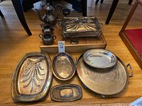 Photo of all silver plated trays, teapot, cups, and warming tray on wooden floor showing tarnish and usage.