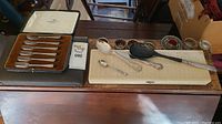Wide view of silver plate forks in box, various hand painted brass utensils and serving spoons arranged on table