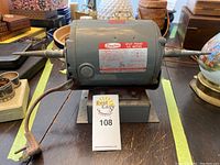 Full view of Dayton gray split phase AC motor showing cylindrical body, shaft at both ends, and attached power cord on wooden table.