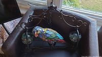 Chandelier with stained glass parrot centerpiece and metal frame seen from above in a box.